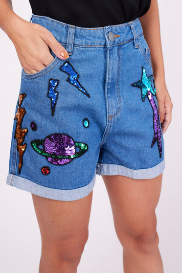 Modelo Marina veste shorts bordado cosmic azul. Peça com bordado manual de paetês e pedrarias que formam diversos desenhos.