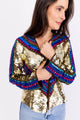Modelo Simone está vestindo casaqueto netuno na cor dourado. Peça com paetês dourados e chatons nas cores: vermelho e azul.