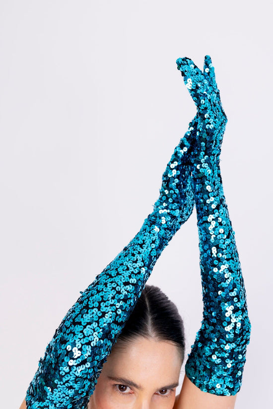 Modelo Simone está com as mãos para o alto enquanto usa a luva bordada luna turquesa. Acessório bordado inteiramente à mão.