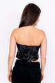 Modelo Simone está de costas e usa top corset sole preto. Top feito inteiramente à mão, possui fechamento de zíper nas costas
