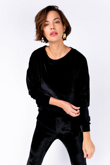Modelo Michela usa blusa velvet na cor preta. Peça super confortável de tecido de veludo, possui manga longa e gola redonda.