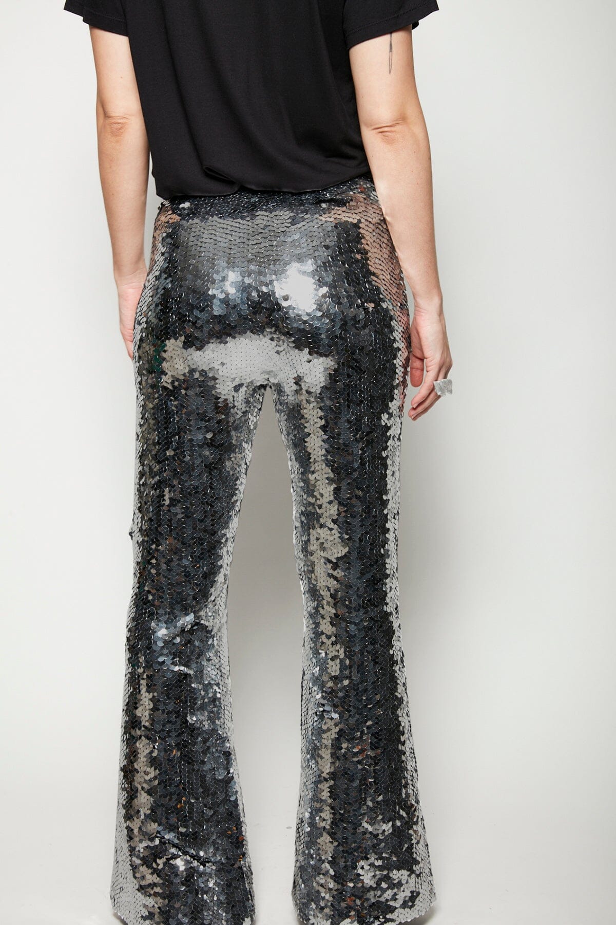 Modelo Isabel está de costas e usa calça flare sole grafite. Peça de malha mais justa nas coxas e vai ficando larga na barra.