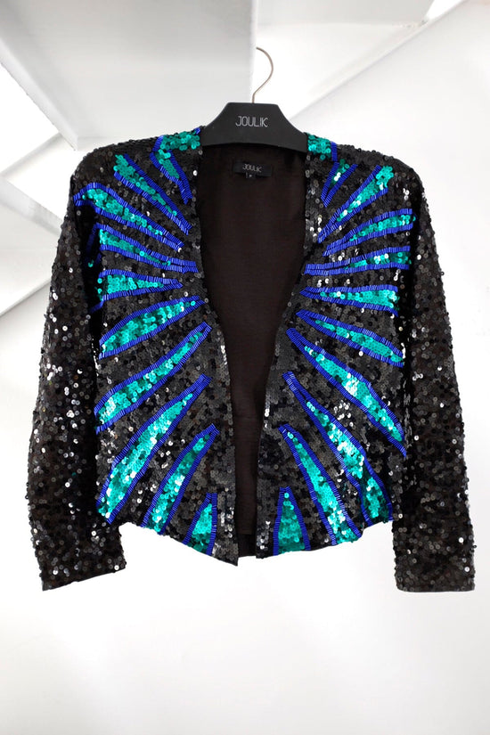 Foto em estilo still do casaqueto ava nas cores azul e verde. Peça com bordado feito à mão de paetês. Produzida no Brasil.