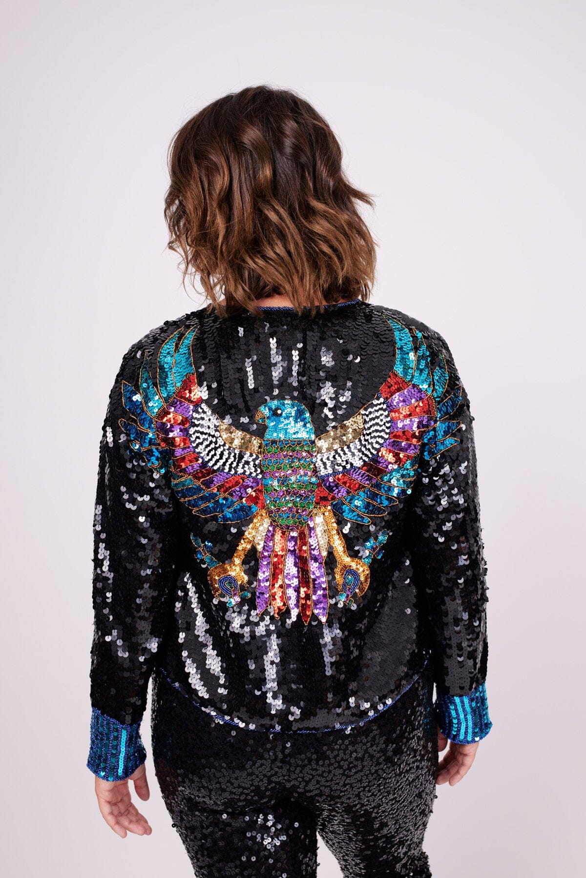 Modelo Victoria está de costas e usando casaqueto bordado falcon. Peça ideal para usar em jantares, festas, shows ou eventos.