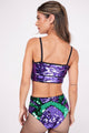 Modelo Marina está de costas e usando hot pant bordada frevo roxo e verde. Peça de malha com bordado feito à mão de paetês.