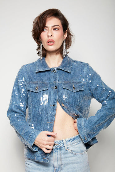 Modelo Isabel está vestindo jaqueta jeans bordada vitru azul. Peça com bordado manual de de paetês escamados transparente.