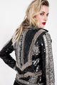 Modelo Juliana está de costas e usando jaqueta perfecto bordada kim. Peça com muito brilho de paetês preto, spike e pedrarias