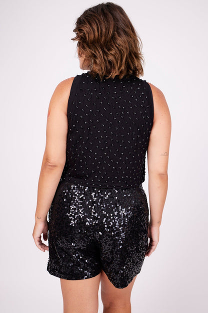 Modelo Victoria está de costas e usa shorts luna preto. Peça com muito brilho de paetês. Ideal para compor looks e arrasar.