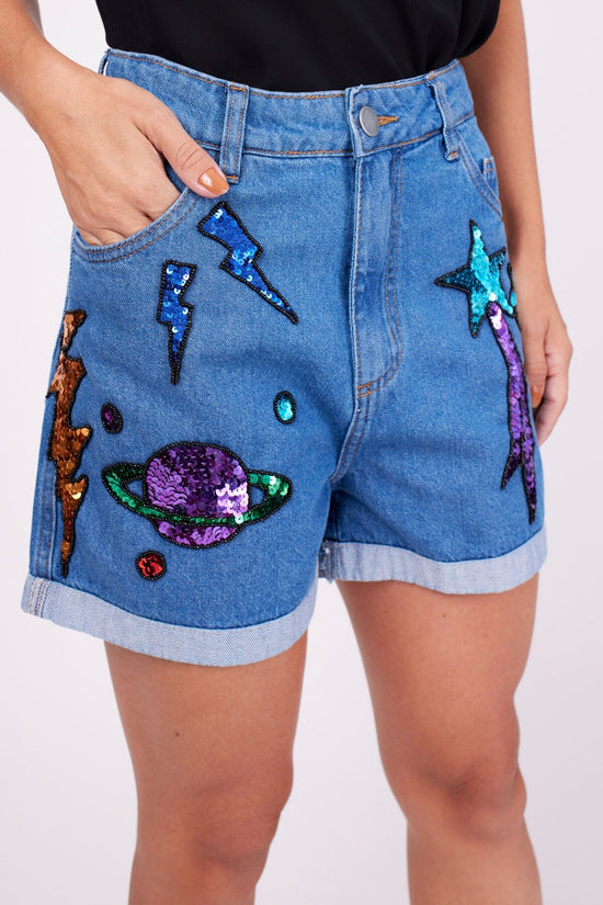 Modelo Marina veste shorts bordado cosmic azul. Peça com bordado manual de paetês e pedrarias que formam diversos desenhos.