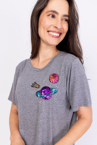 Modelo Simone está vestindo camiseta bordada cosmic na cor mescla. Peça feita à mão com paetês e pedrarias de diversas cores.