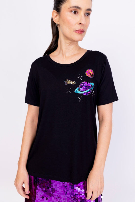 Modelo Simone usa camiseta bordada cosmic na cor preta. Peça com bordado manual na parte superior esquerda de quem veste.