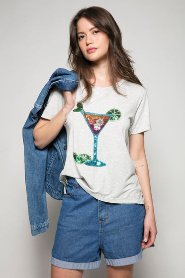 Modelo Ana está vestindo camiseta drink cor mescla. Peça com bordado manual de paetês e pedrarias que forma desenho de taça.