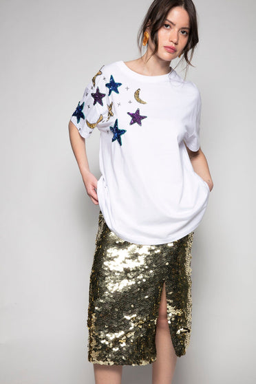 Modelo Ana está usando camiseta estrelas na cor branca. Peça com bordado manual de paetês que formam desenhos de estrelas.