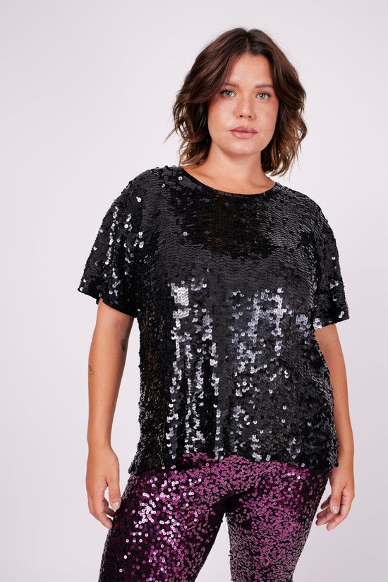 Modelo Victoria está usando camiseta bordada sole na cor preta. Peça de malha com bordado manual de paetês. Feito no Brasil.