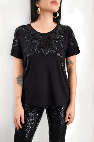 Modelo Katy veste t-shirt texas preta e calça luna preta. Blusa possui bordado à mão de paetês e chatons na parte de cima.