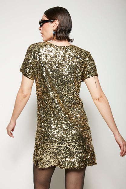Modelo Isabel está de costas e usando vestido luna dourado. Peça com muito brilho de paetês bordados à mão. Feito no Brasil.