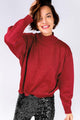 Modelo Michela está usando blusa tricot orion lurex com gola alta vemelha no tamanho P. Peça com efeito de brilho metalizado.