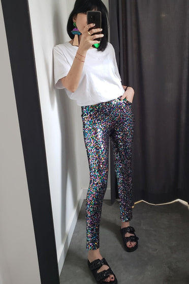 Modelo veste calça skinny luna colorida. Peça bordada manualmente, possui bolsos e muito brilho de paetês salpicado colorido.