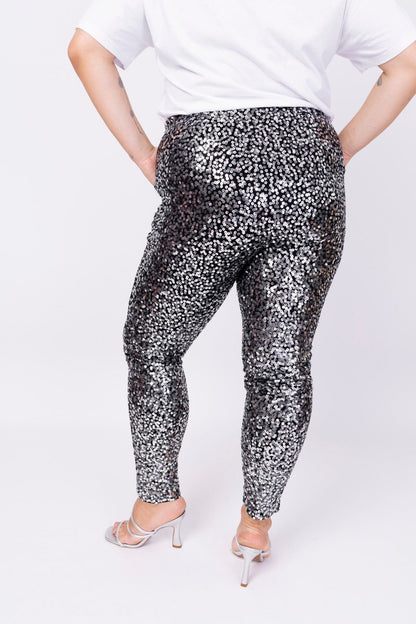 Modelo está de costas e usando calça bordada luna na cor grafite com prata. Peça com bordado inteiramente manual de paetês. 