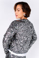 Modelo Michela está de costas e usando casaqueto bordado luna. Peça com bordado manual salpicado na cor prata com grafite.