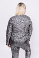 Modelo Victoria está de costas e vestindo casaqueto bordado luna grafite com prata. Possui muito brilho de paetês bordados.