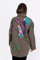 Modelo Simone está de costas e vestindo jaqueta parka beija-flor na cor verde. Peça bordada à mão com paetês e pedrarias.
