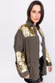 Modelo Simone usa jaqueta parka gama dourada. Peça possui bolsos e fechamento por zíper de metal. Modelagem estilo oversize. 
