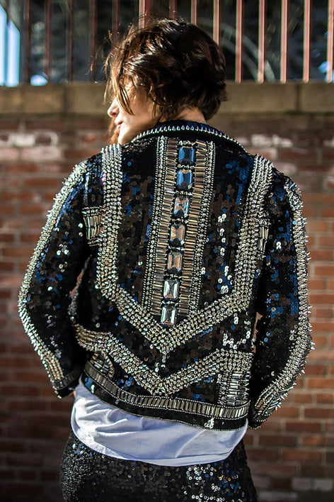 Modelo está de costas e veste jaqueta perfecto bordada Kim cor preto. Peça com paetês, chatons e spikes bordados manualmente 