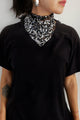 Modelo usa lenço bordado luna nas cores mix grafite com prata no pescoço e camiseta preta. Acessório com brilho de paetês.