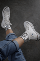 Modelo veste tênis com a meia bordada luna mescla com prata. Possui bordado salpicado nos tornozelos com paetê na cor prata.