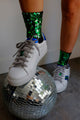 Meia Bordado Luna em uso no pé com bordado feito à mão nos tornozelos de paetês na cor verde. Peça confortável e brilhante.
