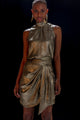 Modelo em pé usando conjunto Atenas. Regata de gola alta confortável, confeccionada com tecido metalizado na cor dourado.