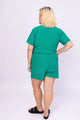 Modelo Victoria está de costas e vestindo conjunto luxor na cor verde. Shorts de malha lurex confortável com muito brilho.