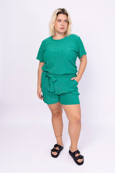 Modelo Victoria está em pé e usa conjunto luxor de malha lurex verde. Shorts possui bolsos frontais e faixa no mesmo tecido.