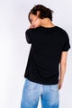 Modelo Michela está de costas e veste a blusa de malha bowie preta. Peça super confortável, é ideal para usar diariamente.