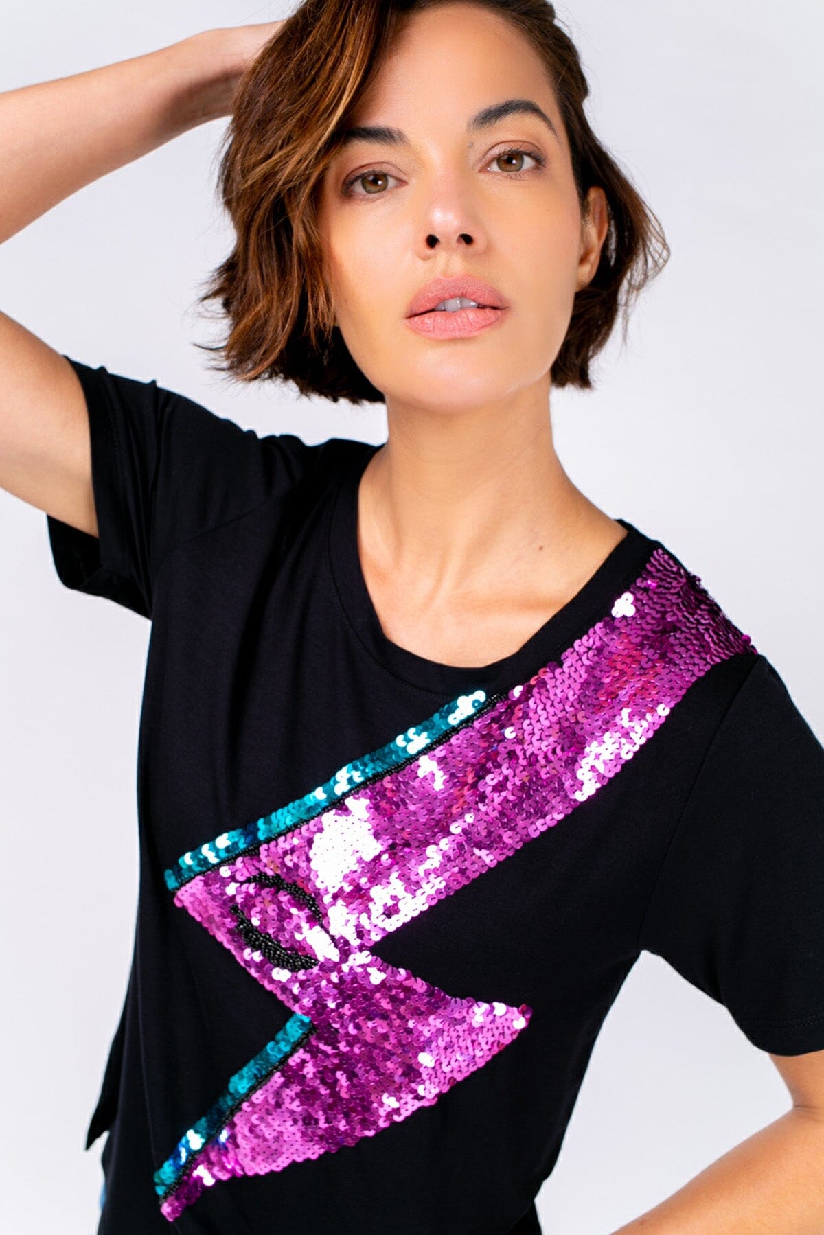 Modelo Michela veste blusa bowie preta. Peça possui um desenho de raio bordado com paetês. É ideal para usar em eventos.
