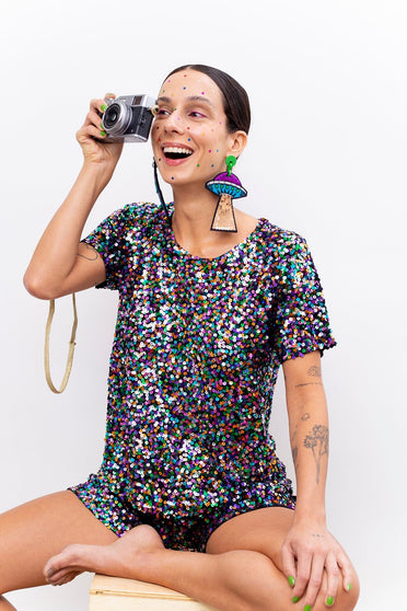 Modelo sorrindo e segurando a câmera enquanto usa Tshirt Luna Joulik com paetês colorido. Peça bordada à mão. Origem nacional