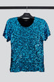 Foto em estilo still da blusa Luna com paetês de cor turquesa, peça com bordado manual, ideal para usar em festas e eventos.