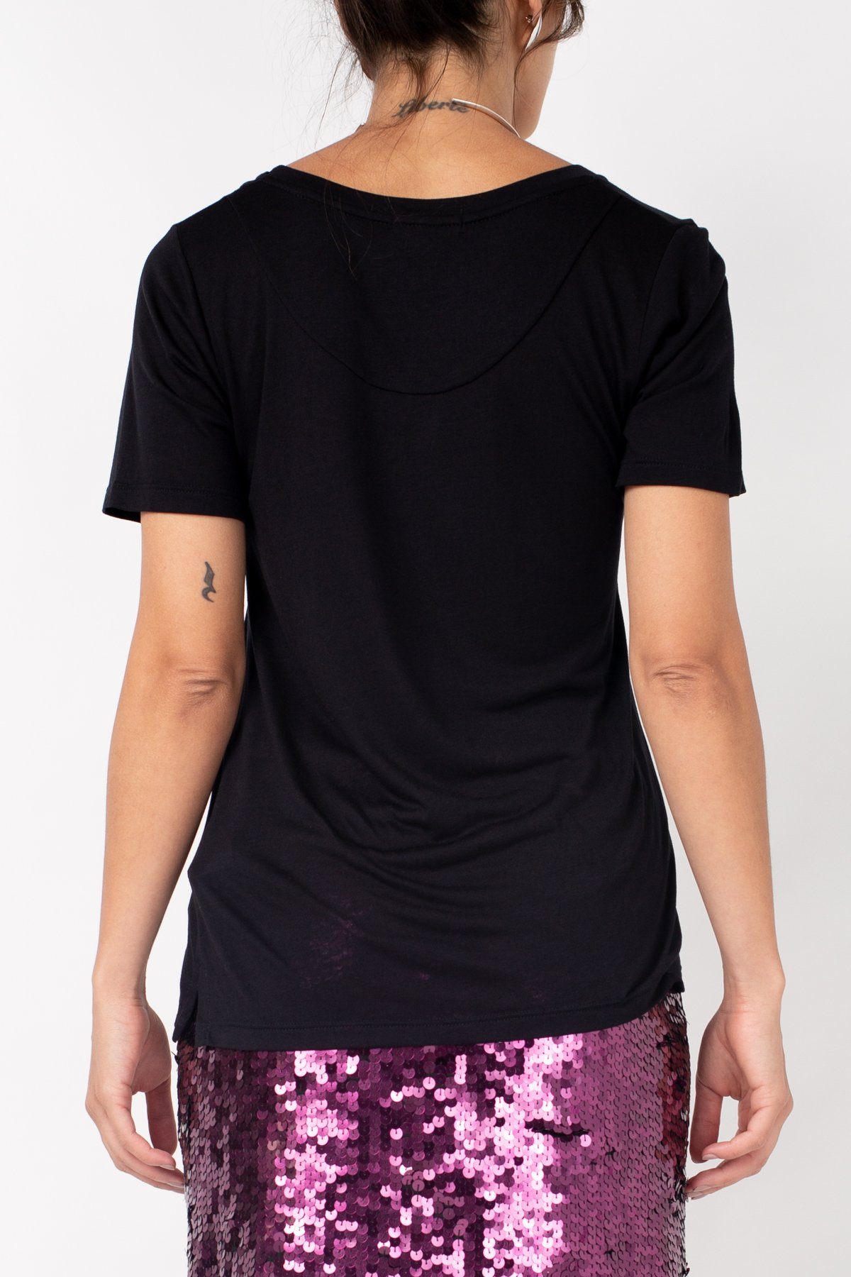 Modelo Nat está de costas e usando blusa preta básica. Peça ideal para usar com acessórios para ir em festas ou eventos.