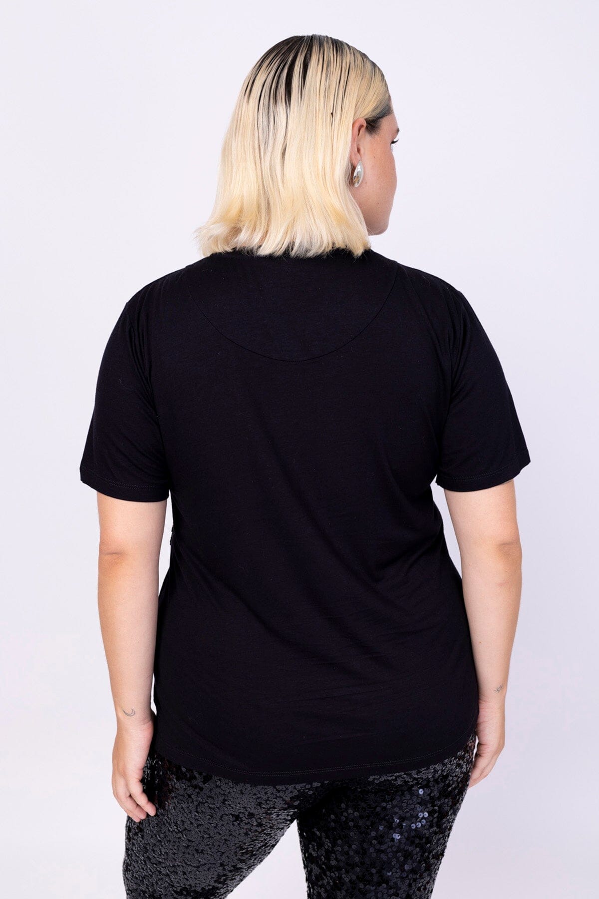 Modelo Victoria está de costas e vestindo blusa básica na cor preta. Peça super confortável, ideal para usar com calça luna.